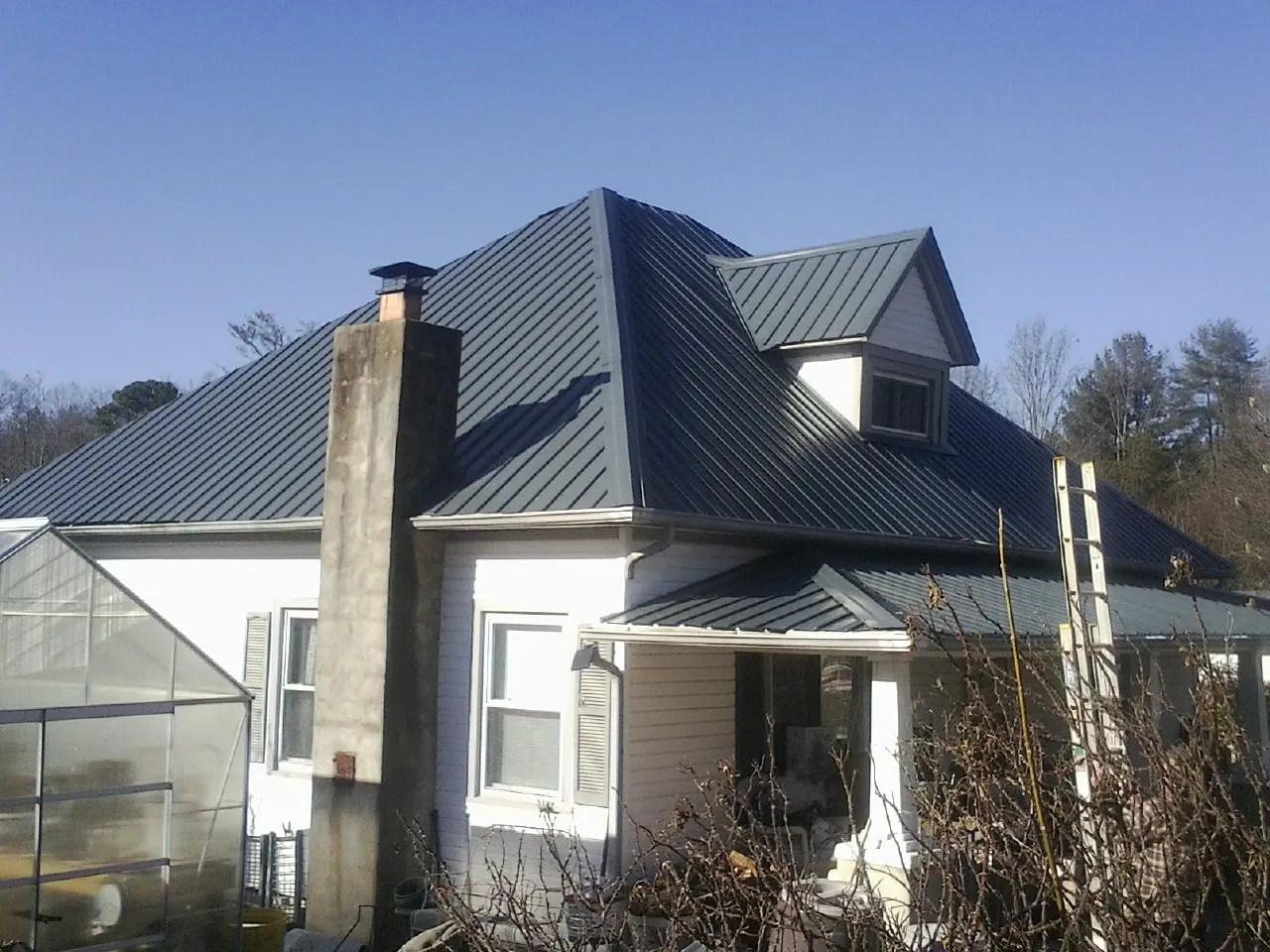 Dark blue standing seam metal roof on a white farmhouse with dormer — Slate & Tile Roof Repair by Roofing Brothers in Smyrna