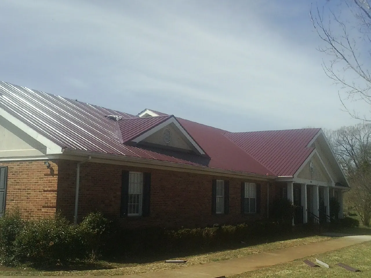 Red metal roof with gabled entries on a long brick building, from a Hail Damage Roof Repair job in Smyrna